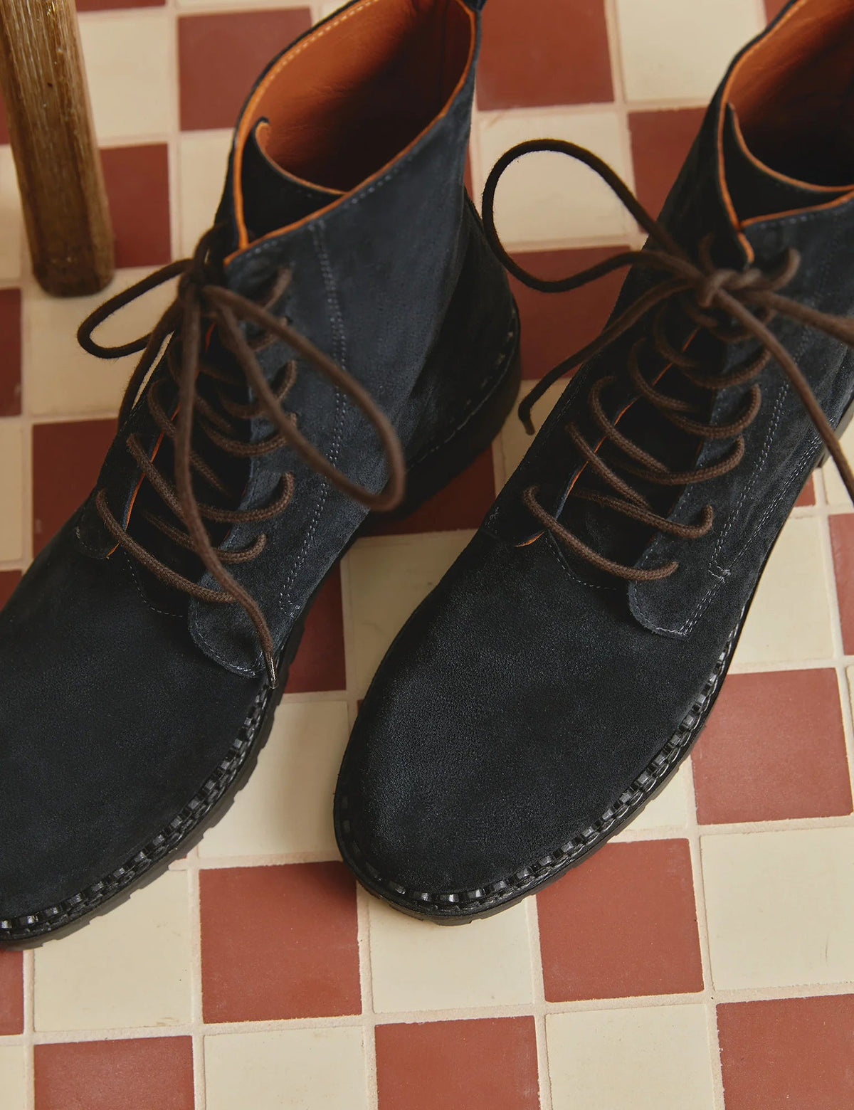 The Copper Shed Bartholomew navy suede lace-up boots with brown laces and scalloped tread soles on a tiled floor.