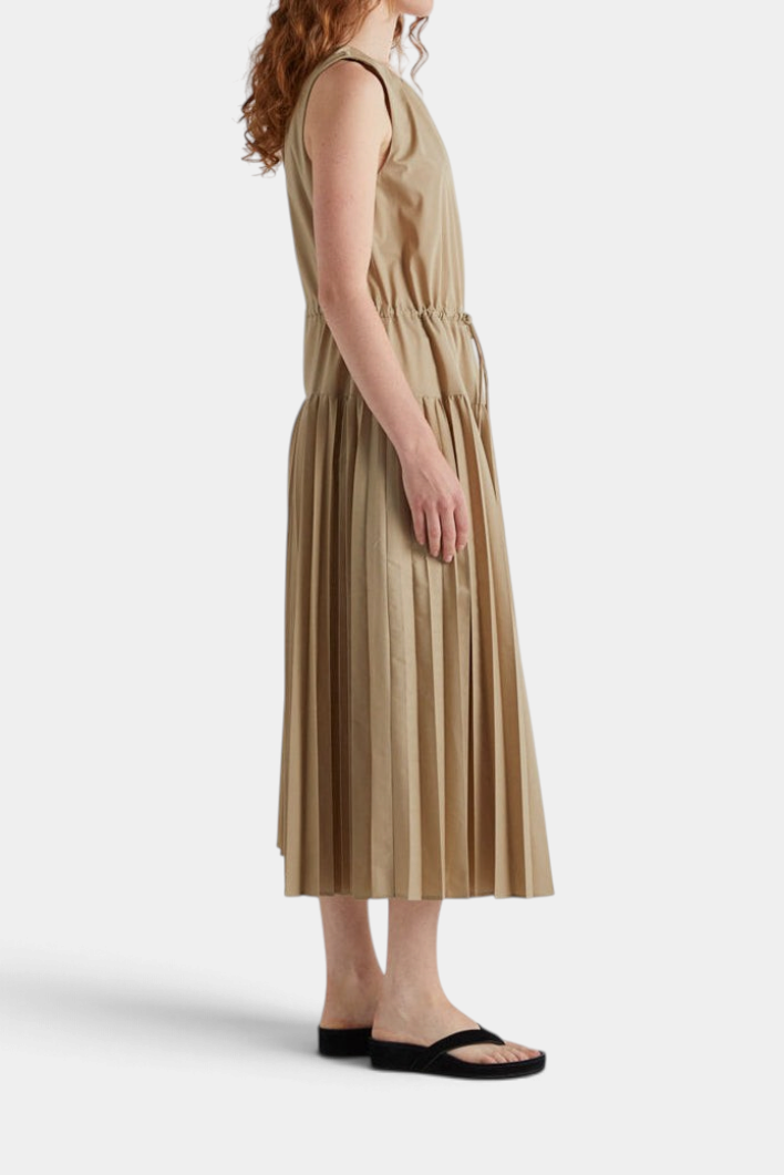 The Copper Shed sleeveless beige long dress with a drawstring waist and pleated skirt, side view on a model.