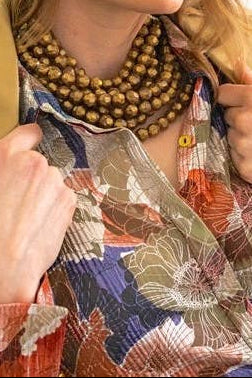 The Copper Shed Bella Holiday gold resin bead layered necklace on a model wearing a patterned floral shirt