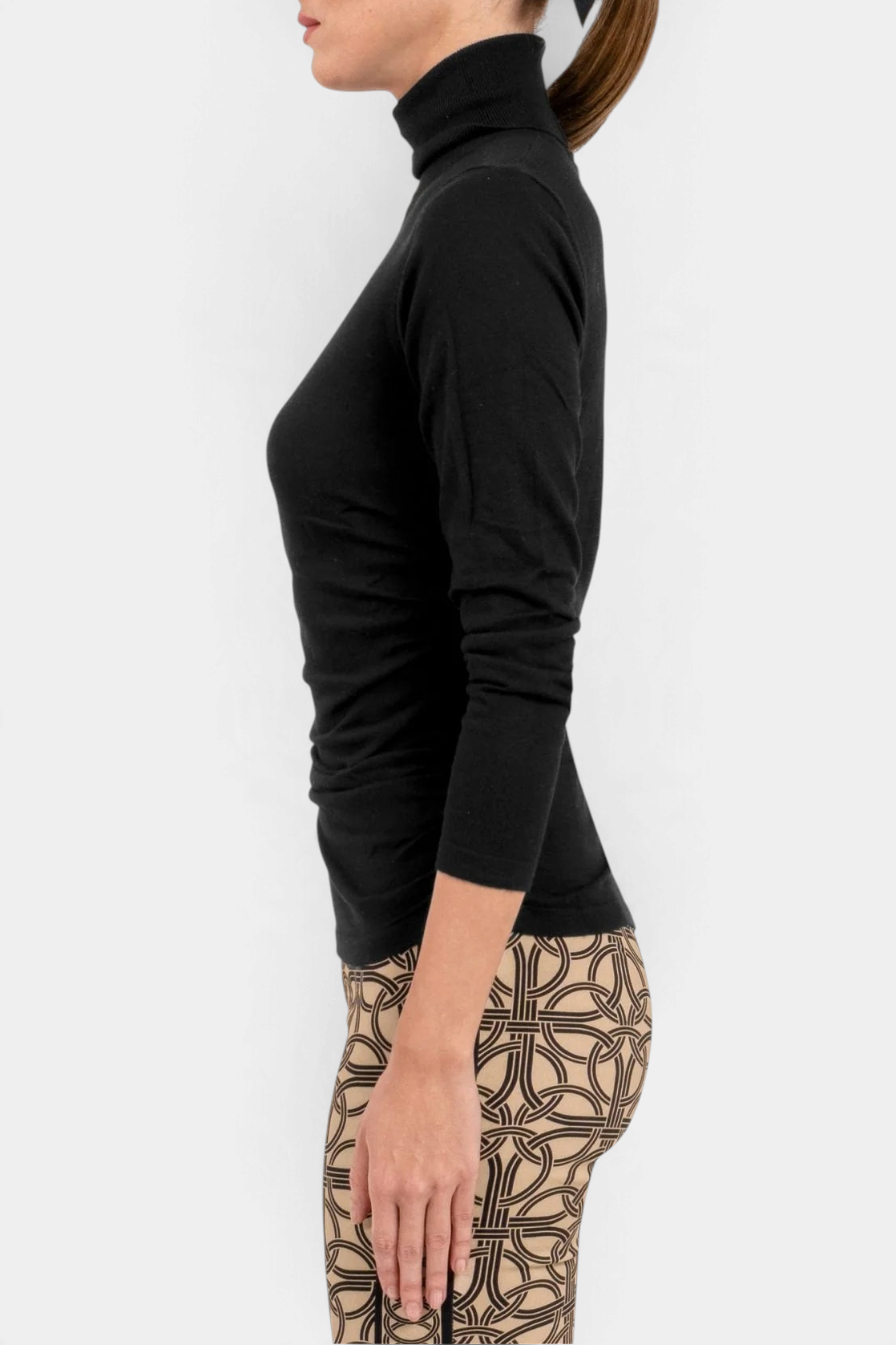 The Copper Shed black cashmere turtleneck sweater worn by a woman in profile view against a white background.