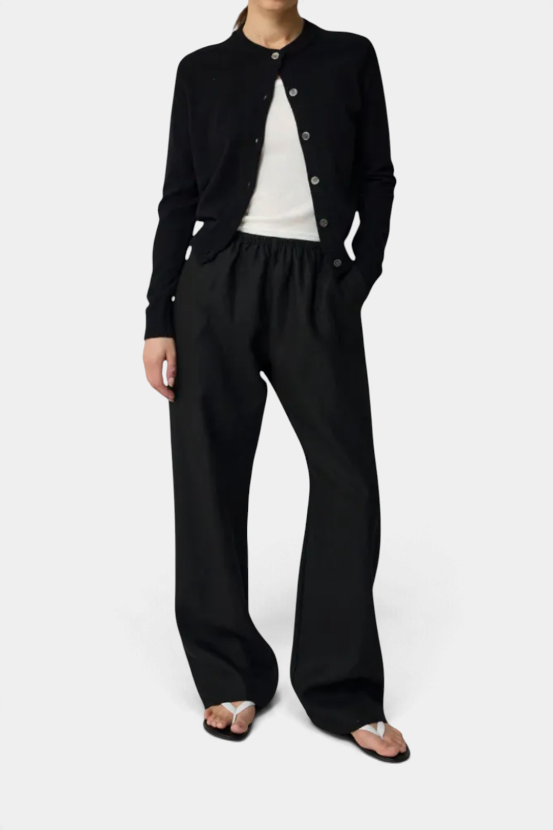 The Copper Shed black crew neck wool blend cardigan worn over a white top with matching black wide-leg trousers.