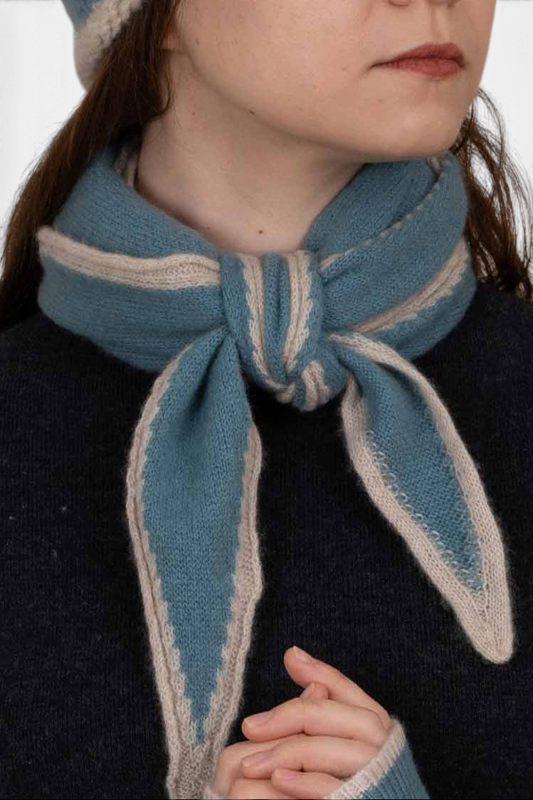 The Copper Shed Austen spindle-shaped blue and beige organic cashmere scarf tied in a stylish French knot