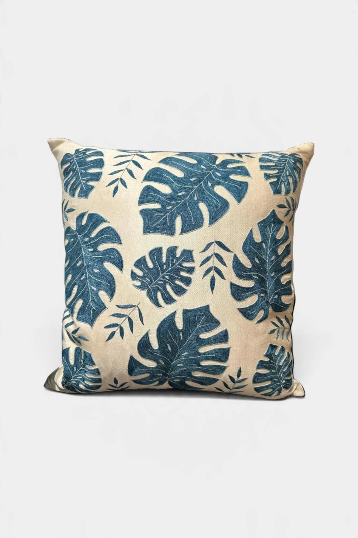 The Copper Shed square throw pillow featuring a blue embroidered palm leaf pattern on a neutral linen-look fabric.