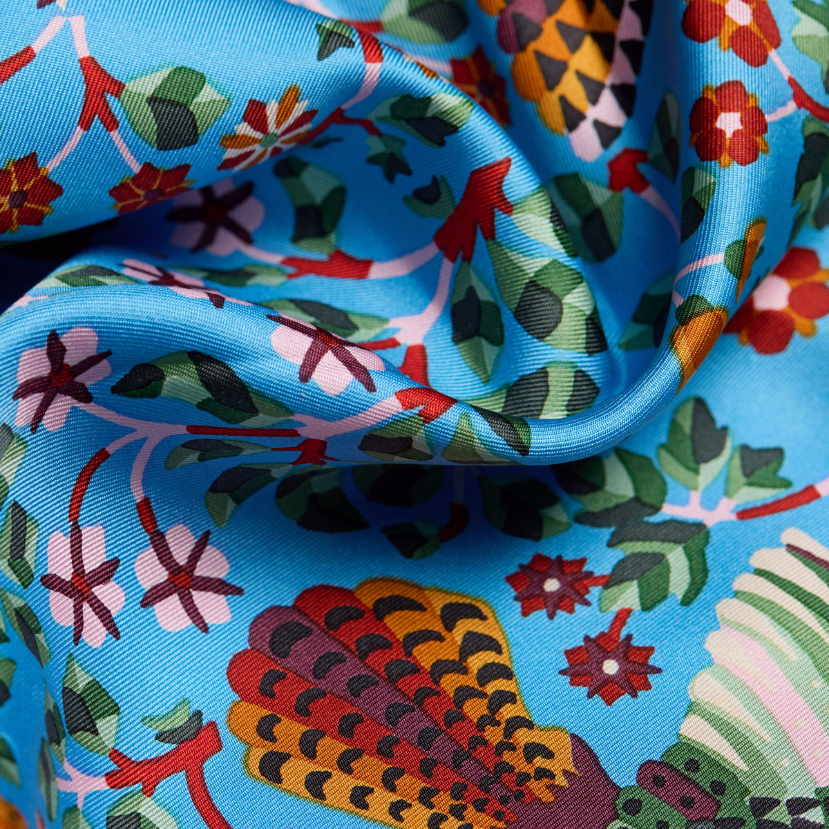 The Copper Shed Perrot blue silk scarf featuring a vibrant floral and bird pattern in a soft, draped fabric.