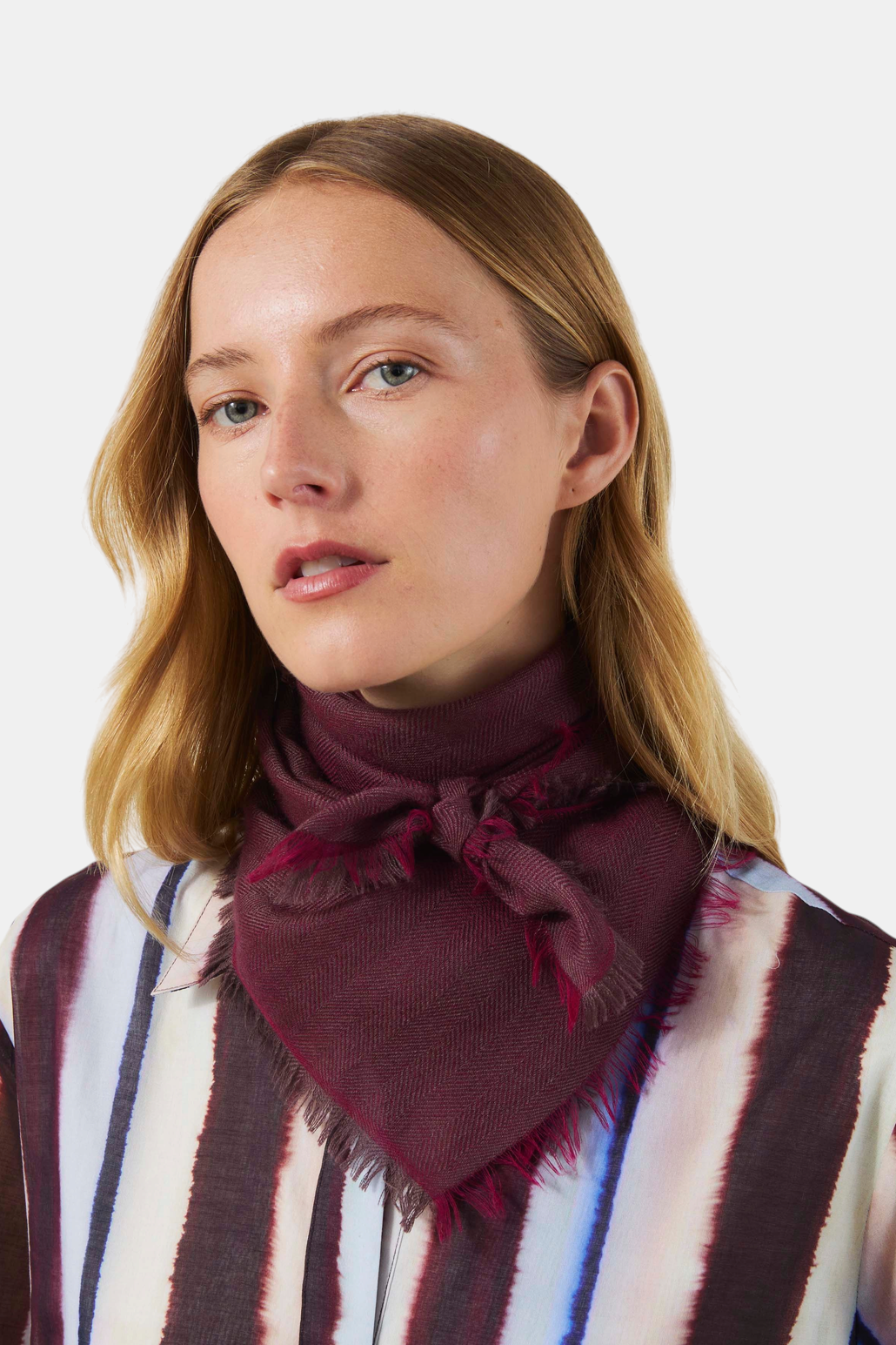 The Copper Shed burgundy cashmere scarf with herringbone pattern and frayed edges worn knotted around the neck.