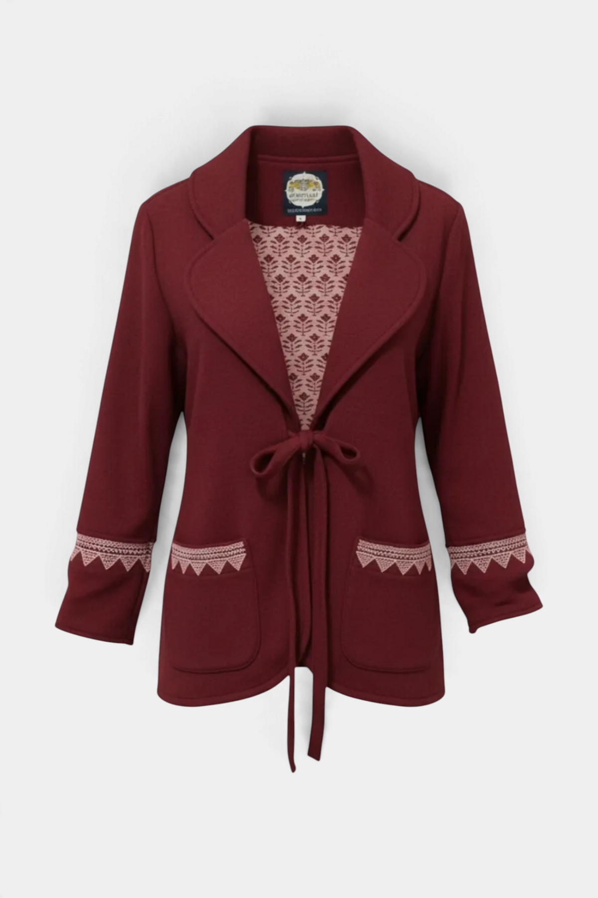 The Copper Shed Leah Jacket in deep burgundy with a tie-front closure, patterned lining, and embroidered pocket trim.