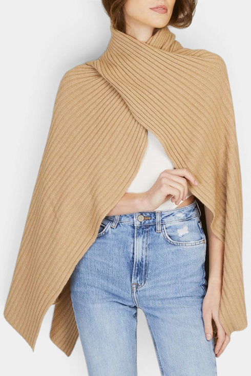 The Copper Shed beige ribbed knit cape with a funnel neckline and handkerchief hem worn over a white top and jeans.