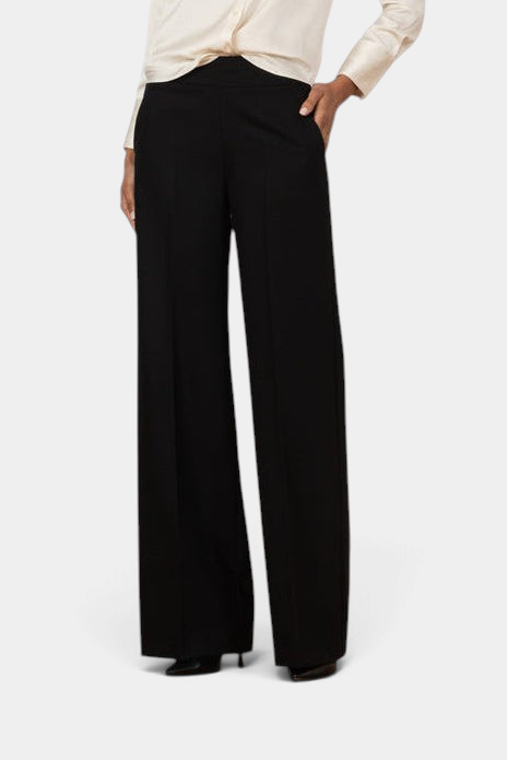 The Copper Shed Carla black palazzo pants with a wide-leg silhouette and side pockets worn with a cream blouse.
