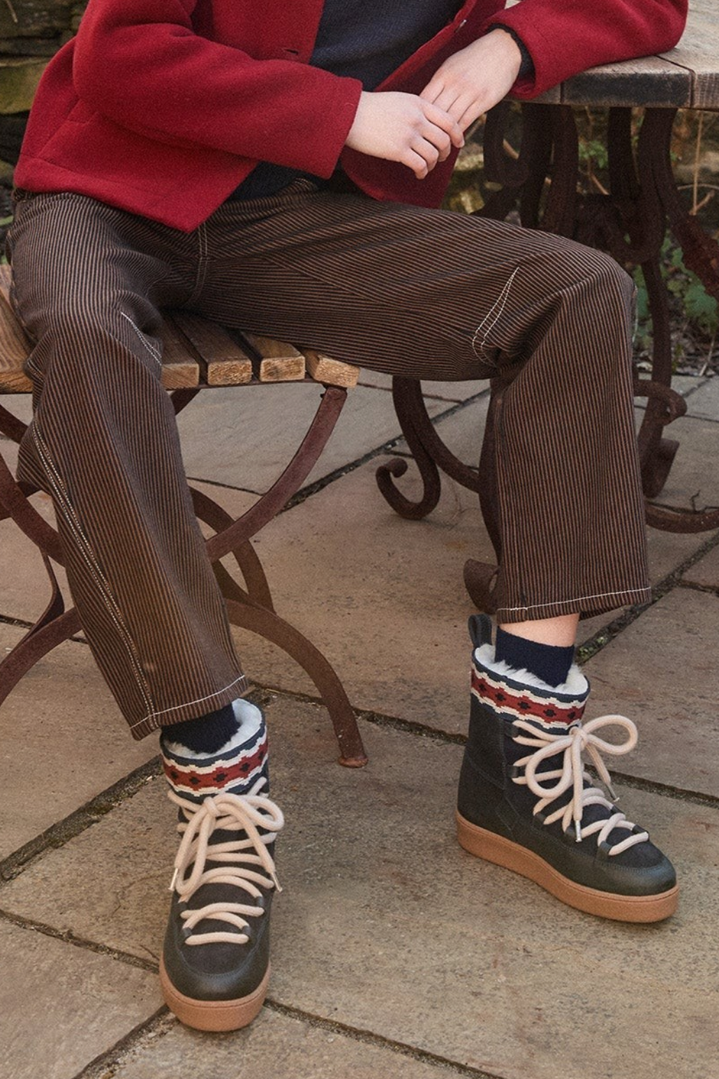 The Copper Shed Cosmo suede moon boots with wool lining, patterned trim, and thick laces worn with brown trousers.