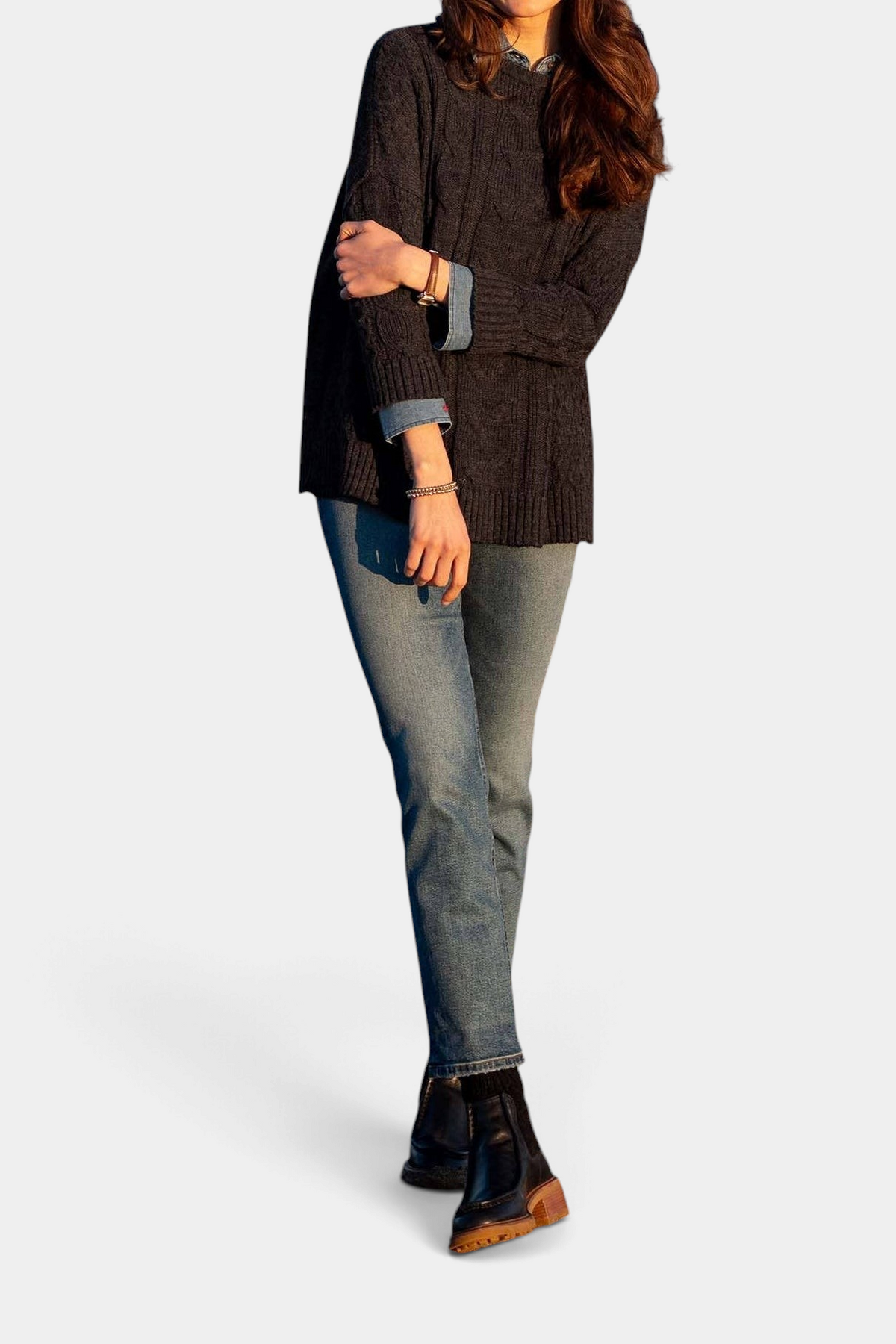 The Copper Shed Cotswold cable-knit sweater in charcoal worn by a model with blue jeans and black boots