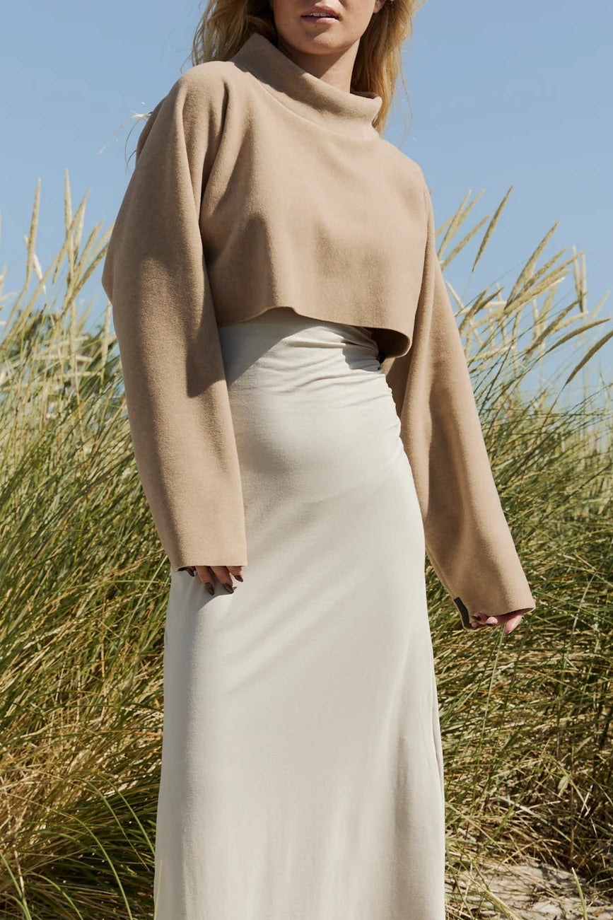 The Copper Shed cropped beige fleece pullover with a roll neck worn over a light dress in a grassy outdoor setting.