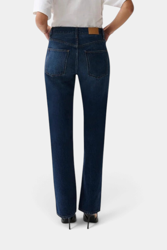 Back view of The Copper Shed Dakota high rise bootcut jeans in dark indigo denim on a model wearing a white top.