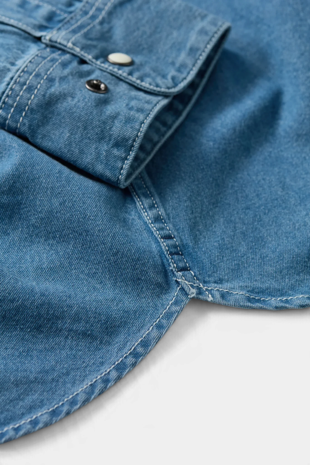 The Copper Shed Westside denim shirt detail showing blue cotton fabric, contrast stitching, and western pearl snaps.