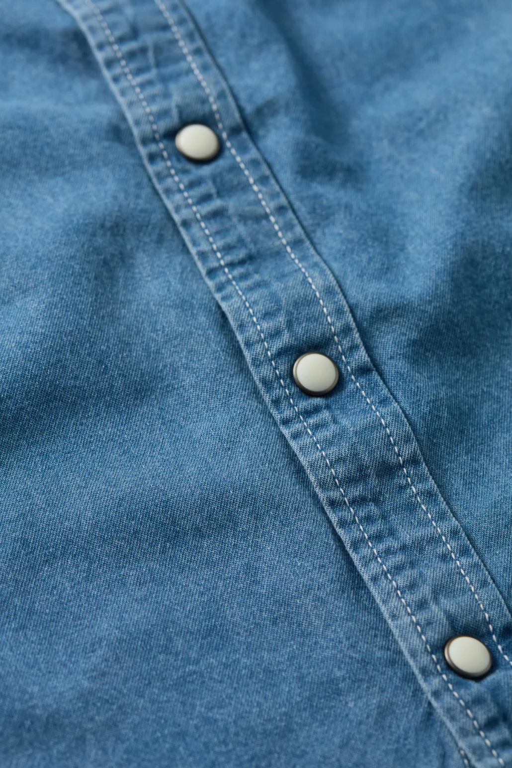 The Copper Shed Westside denim shirt featuring blue garment-dyed cotton fabric and white western pearl snap buttons.