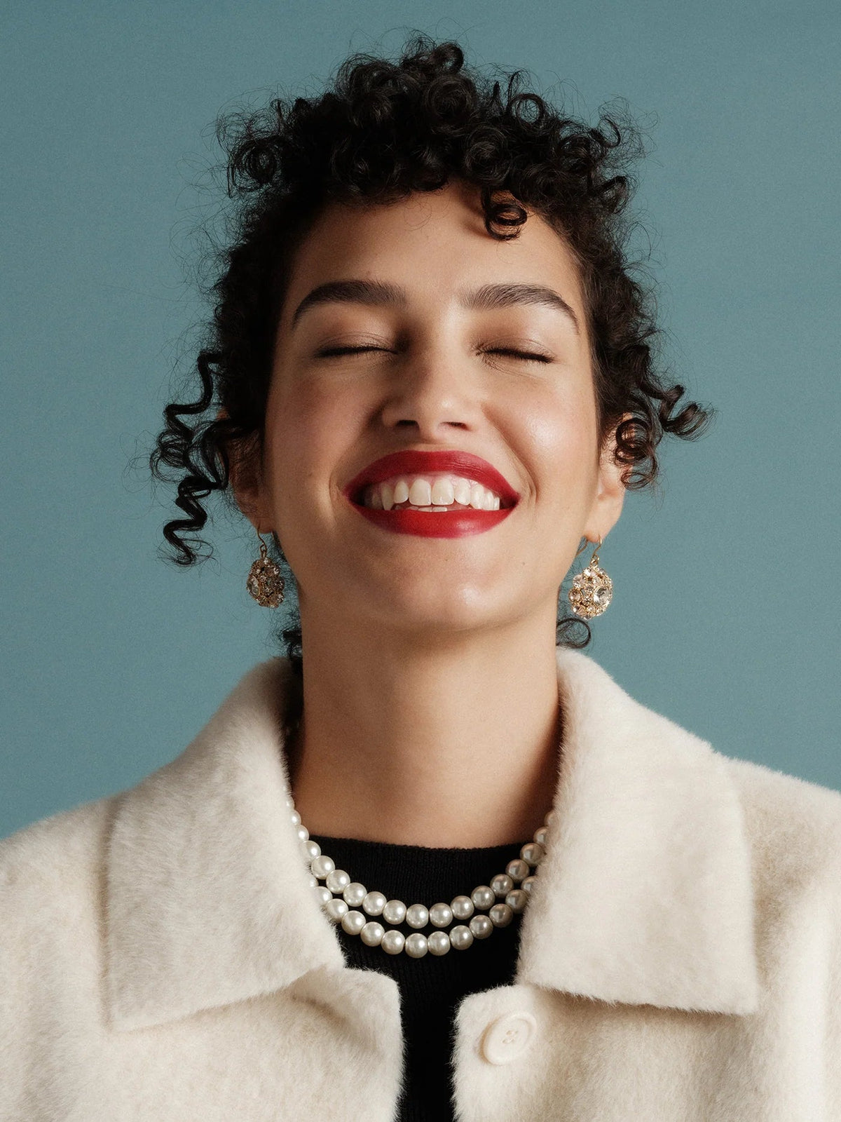 The Copper Shed double strand pearl necklace worn by a smiling woman with curly hair and a cream coat
