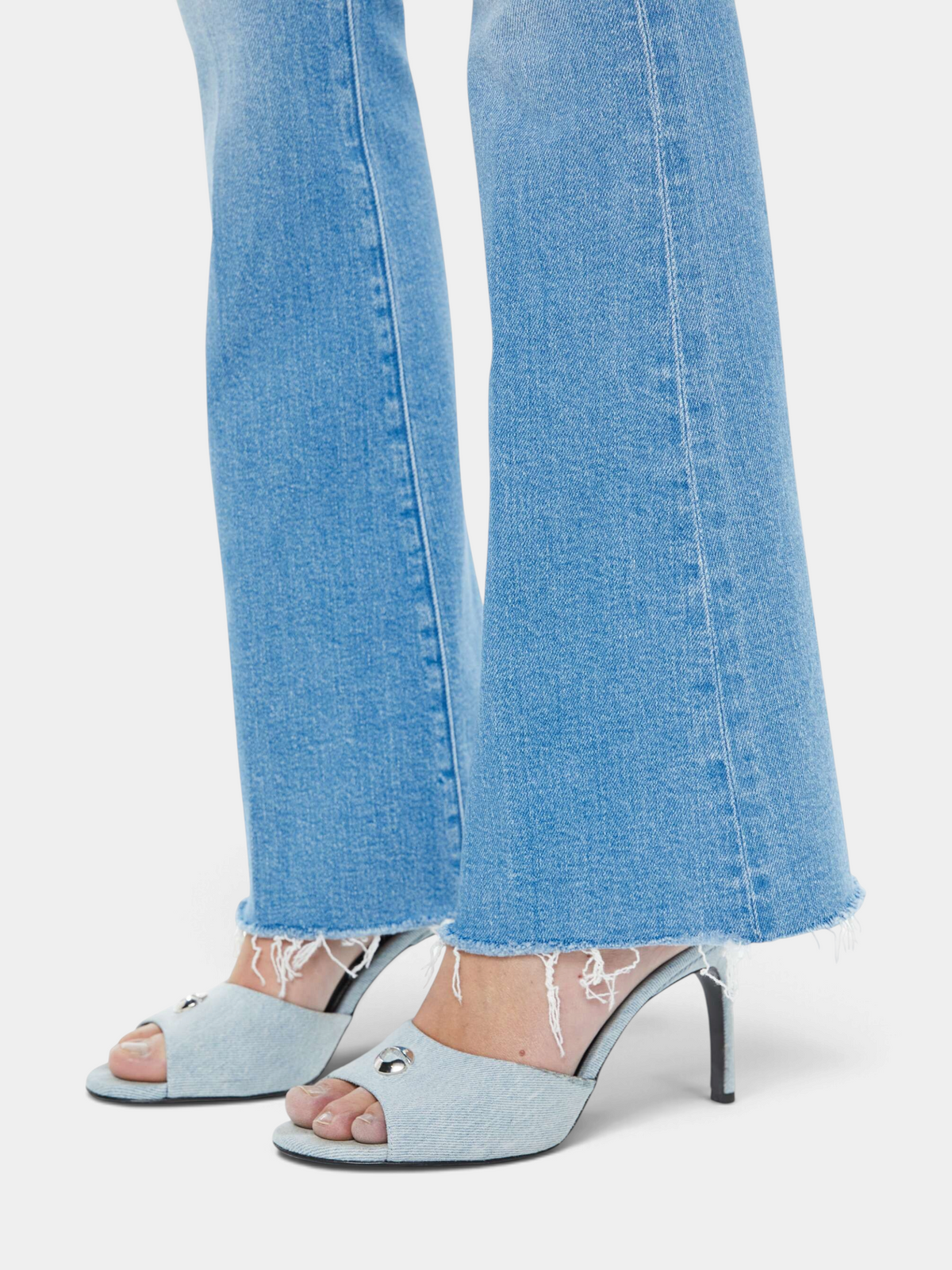 The Copper Shed light blue mid-rise flare jeans with a frayed hem and subtle whiskering on a model wearing heels.