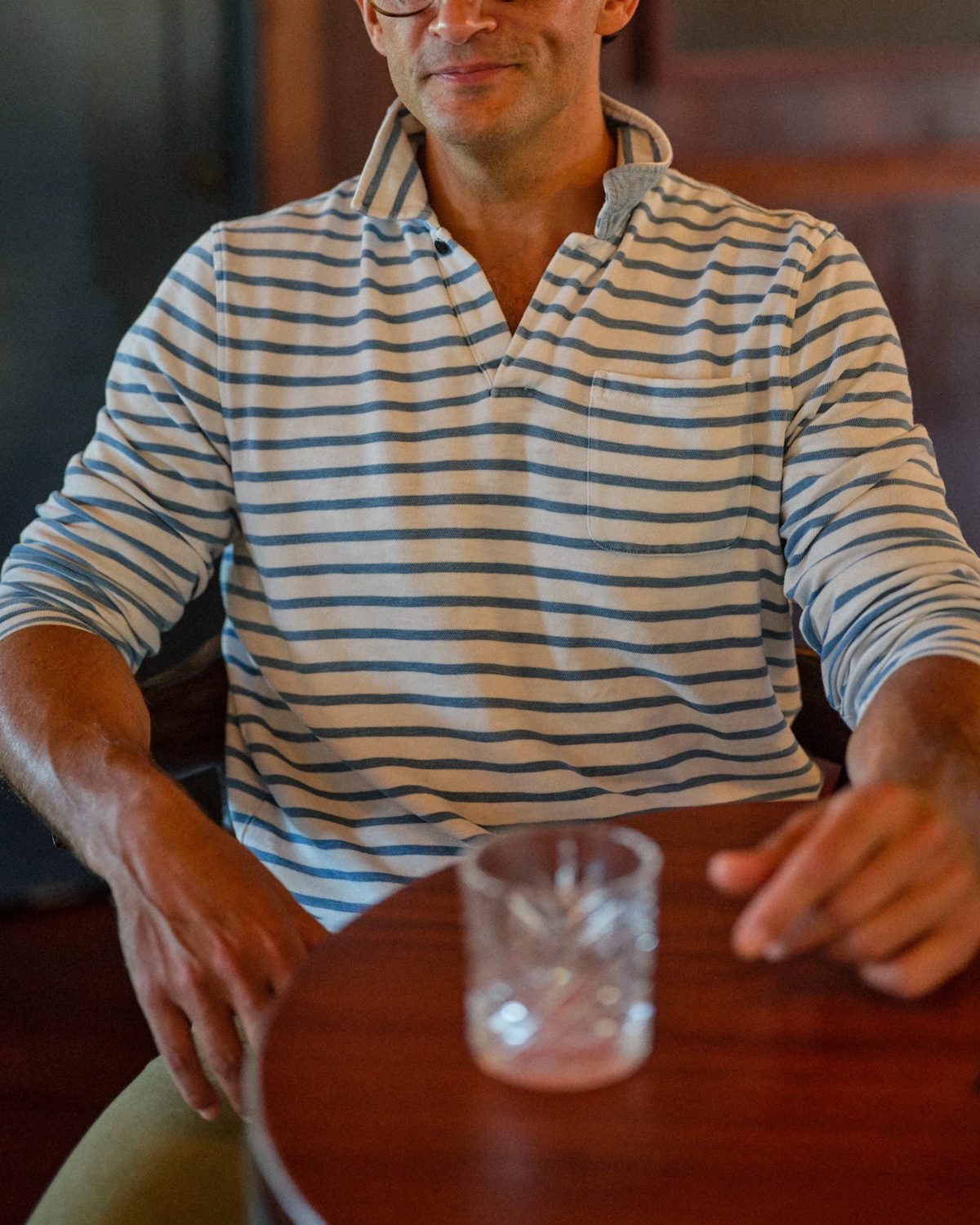 A man wearing The Copper Shed long sleeve indigo striped cotton polo shirt with a one-button collar and chest pocket.