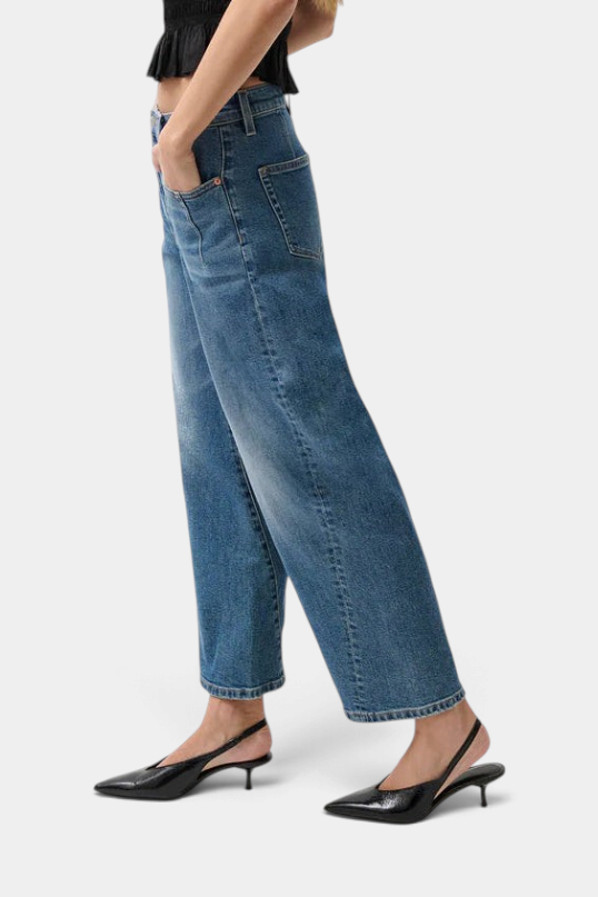 The Copper Shed Kyra high rise bowed ankle jeans in a light vintage wash with twisted seam detail on a model.