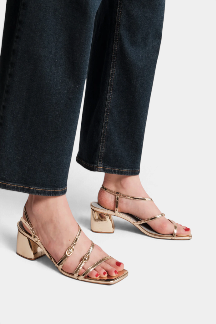 The Copper Shed Lexi gold vegan leather slingback sandals with double straps and a chunky block heel on a model.