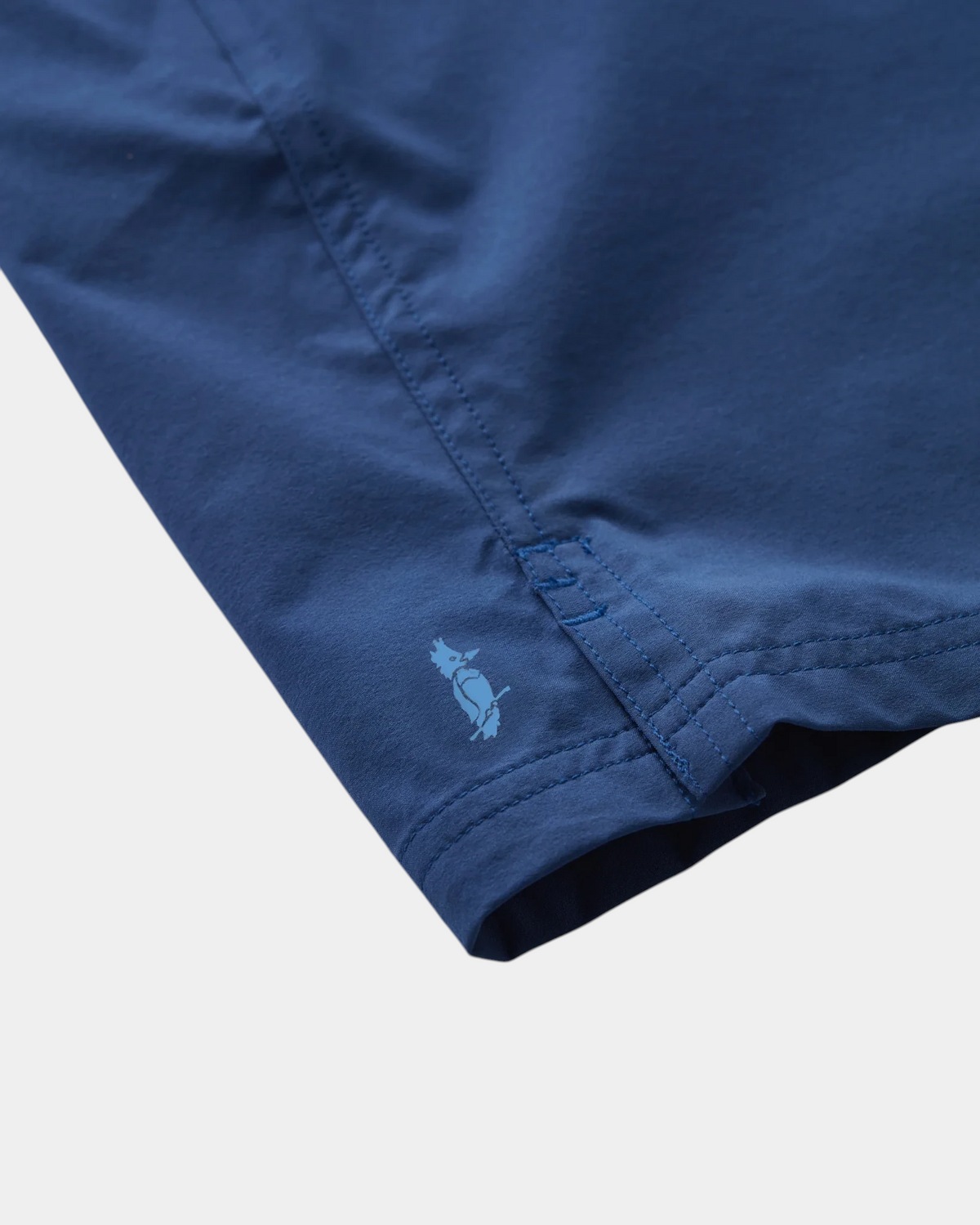 Close-up of The Copper Shed Migration Drawcord short in navy blue featuring a small embroidered bird logo on the hem