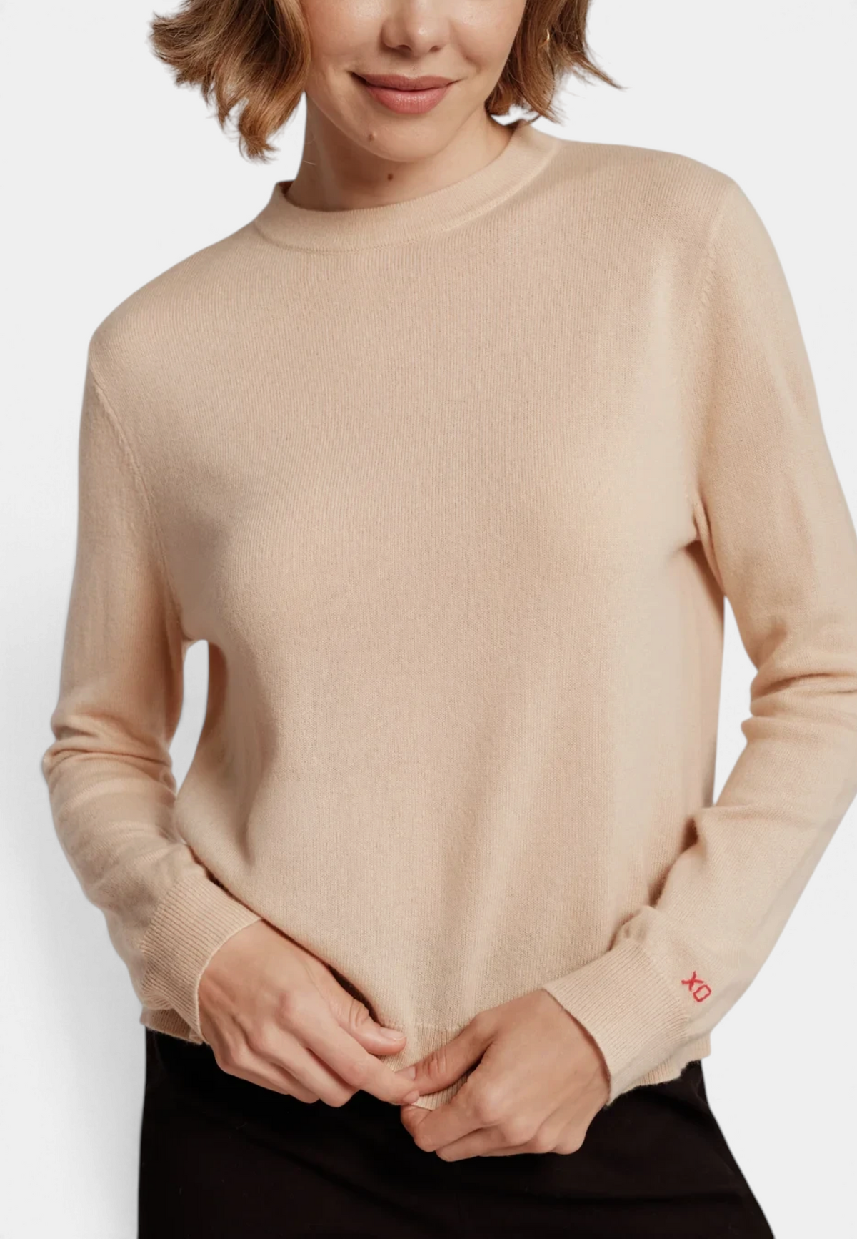 The Copper Shed Mila merino wool sweater in beige with a high neckline and red embroidered detail on the cuff.