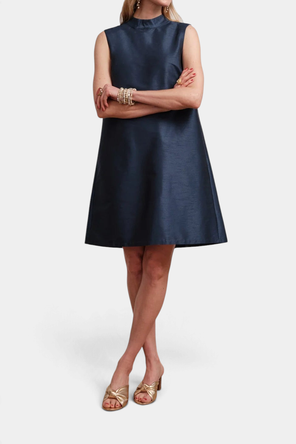 The Copper Shed sleeveless navy blue mini dress with a mock neckline, worn by a model with gold heels.
