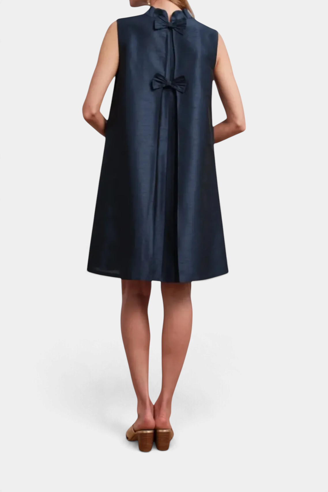 The Copper Shed navy blue sleeveless mini dress featuring a mock neckline and two back bows with pleated detailing.