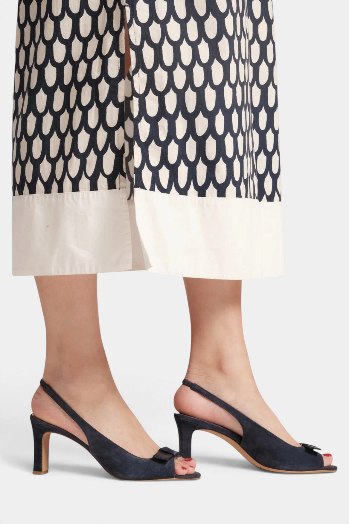 The Copper Shed Reese navy suede slingback heels with bow detail and open-toe design worn with a patterned midi skirt.