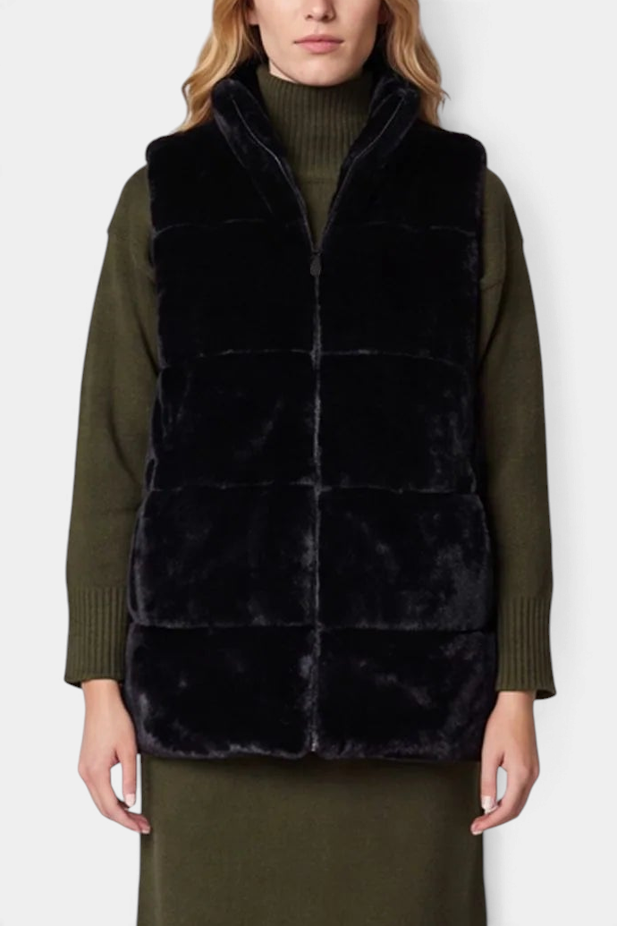 The Copper Shed Nives reversible black faux fur vest with a stand-up collar and front zipper worn over a green dress.