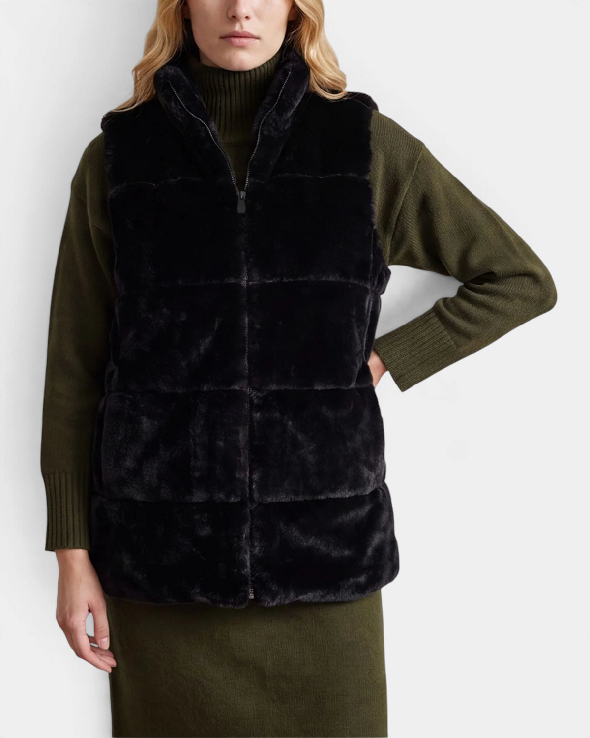 The Copper Shed Nives reversible black faux fur vest with stand-up collar and front zipper worn over olive sweater