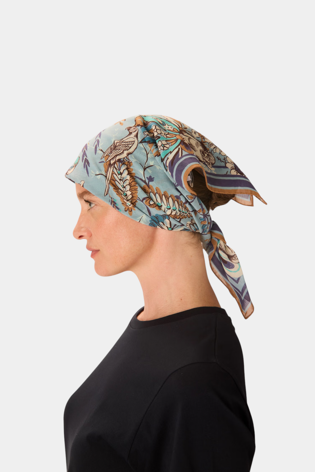 The Copper Shed Square 70 Pagode cotton scarf in blue with intricate bird and floral print worn as a headscarf