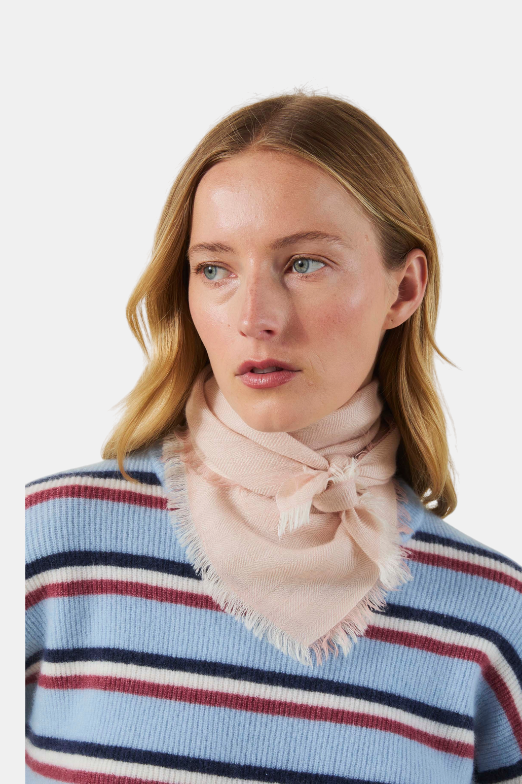 The Copper Shed light pink cashmere scarf with a herringbone pattern and frayed edges worn around the neck.