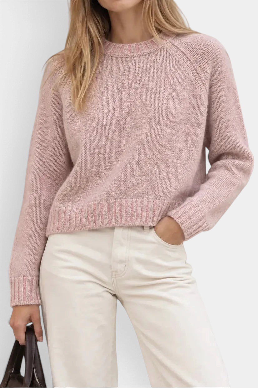 The Copper Shed pink merino wool and cashmere plaited raglan crewneck sweater worn by a model with cream trousers.