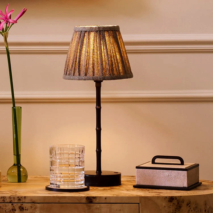 The Copper Shed rechargeable bamboo lamp with a bronze finish and a textured fabric shade on a wooden table.