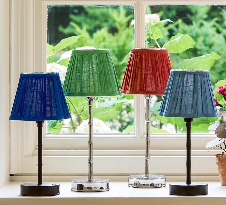 The Copper Shed set of four pleated scalloped lampshades in blue, green, orange, and grey on metal lamp bases.