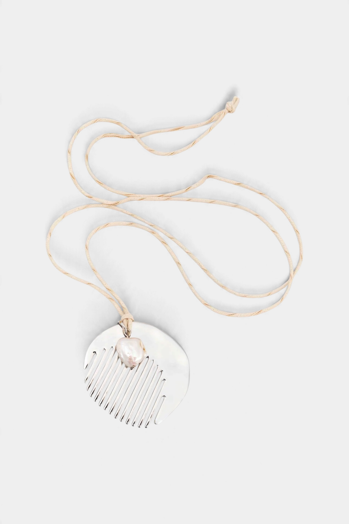 The Copper Shed long necklace featuring a silver-plated zamak comb pendant accented with a natural pearl on a silk cord