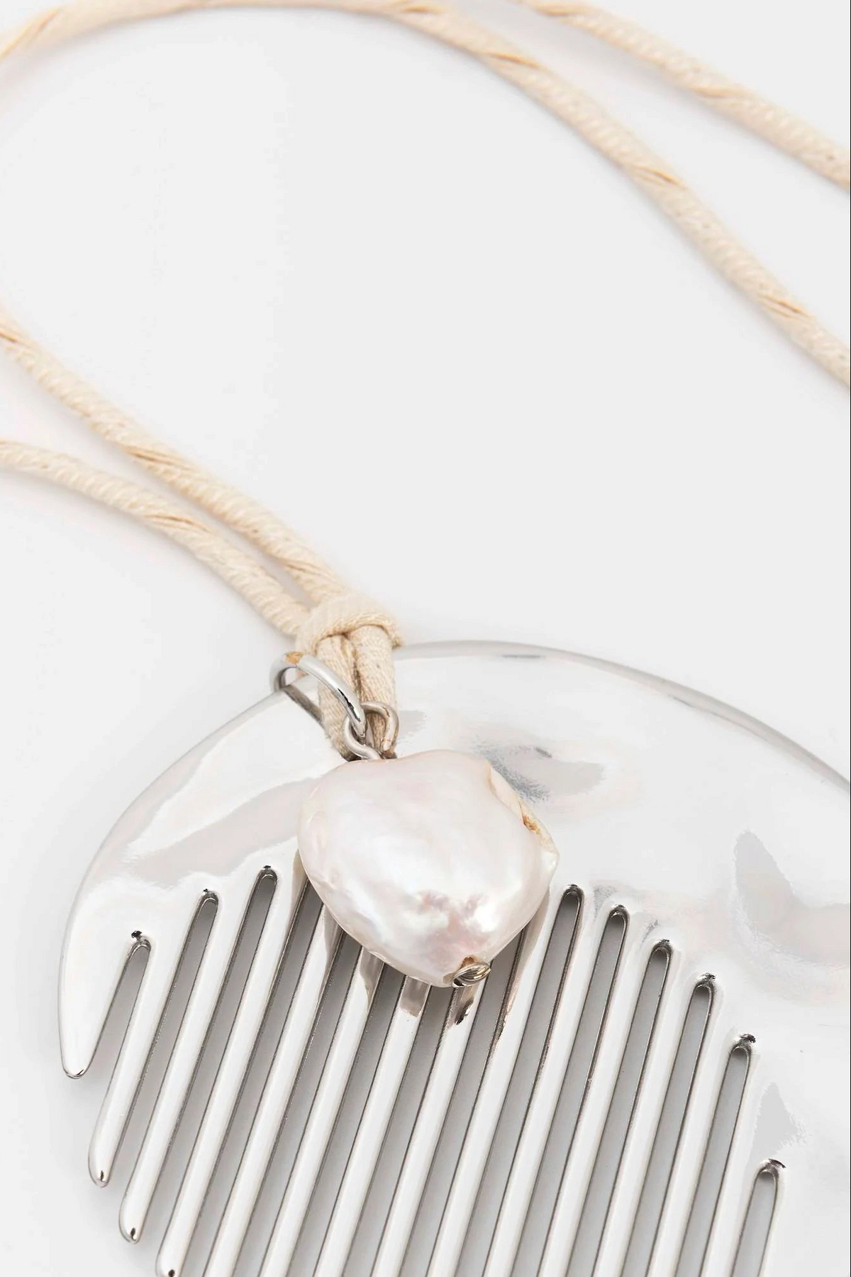 The Copper Shed long necklace featuring a silver-plated zamak comb pendant and a natural pearl on a beige silk cord.