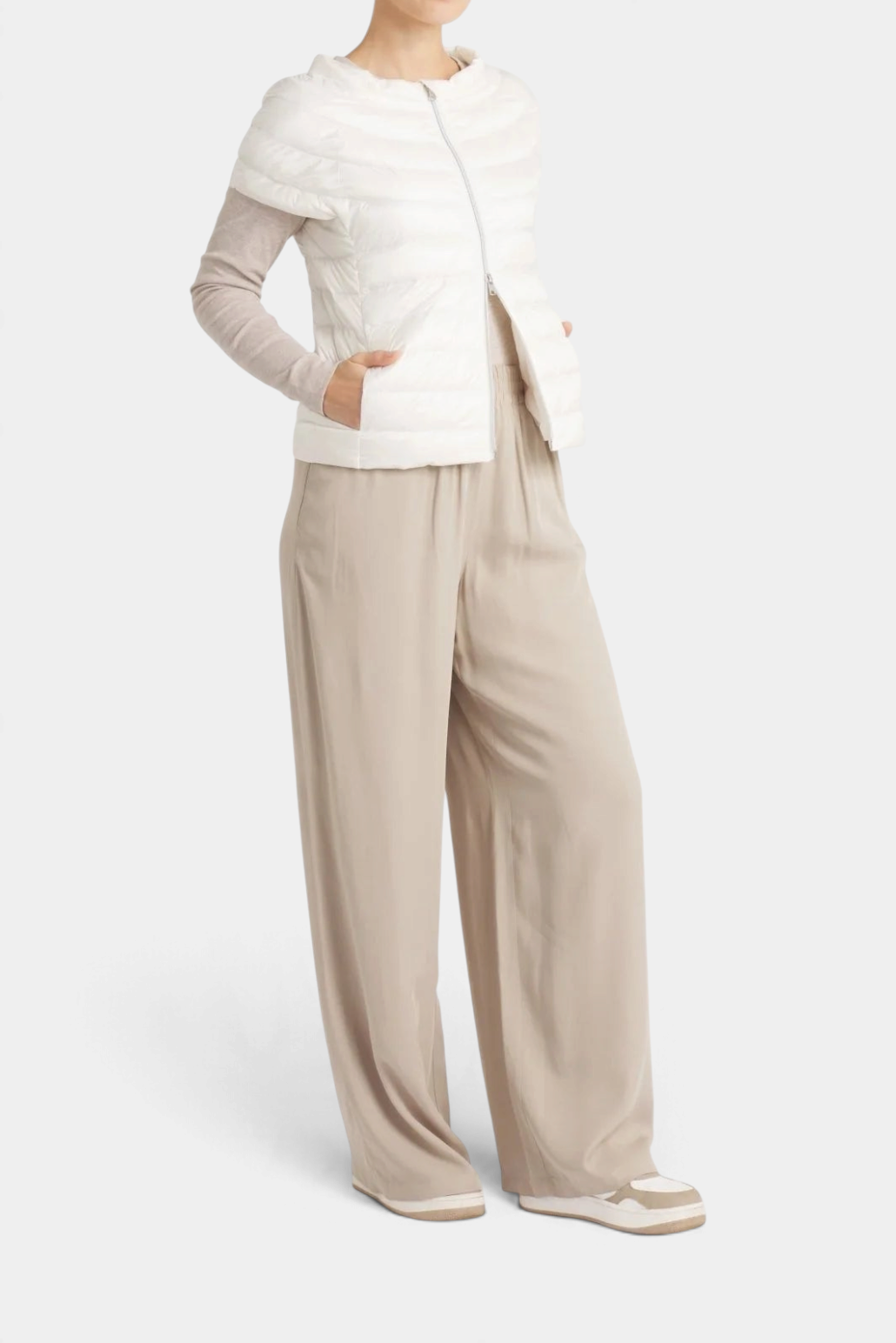 The Copper Shed St Ives white down vest with quarter sleeves worn over a beige long-sleeve top and wide-leg trousers.