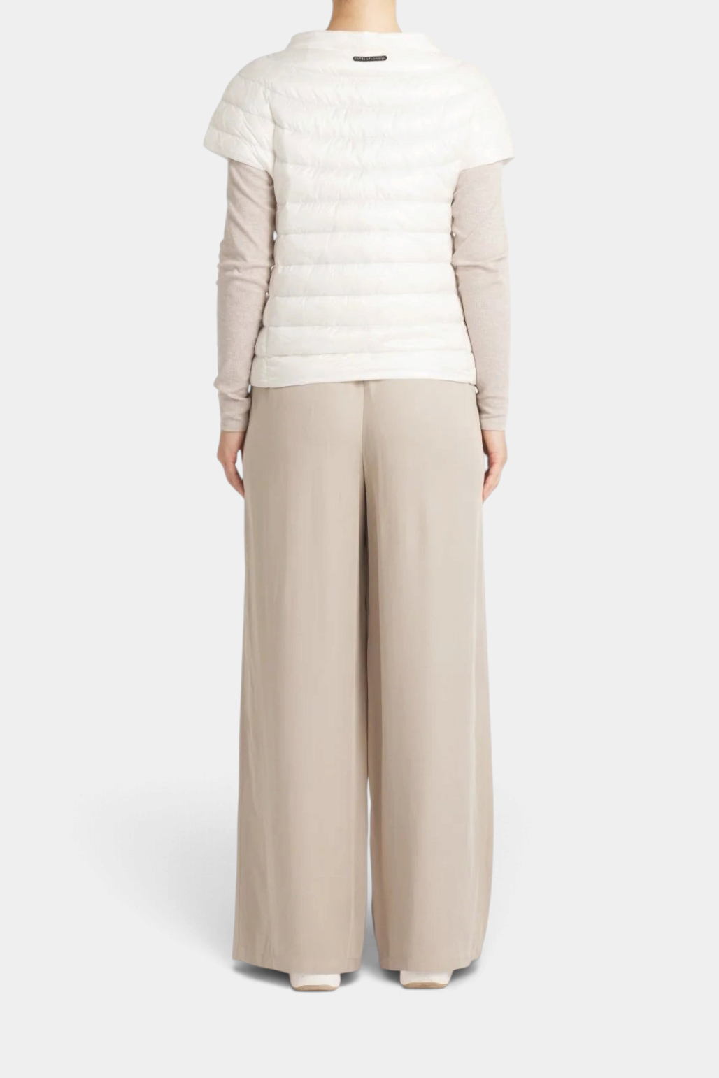The Copper Shed St Ives white down vest with quarter sleeves worn over a beige long sleeve top and wide leg trousers