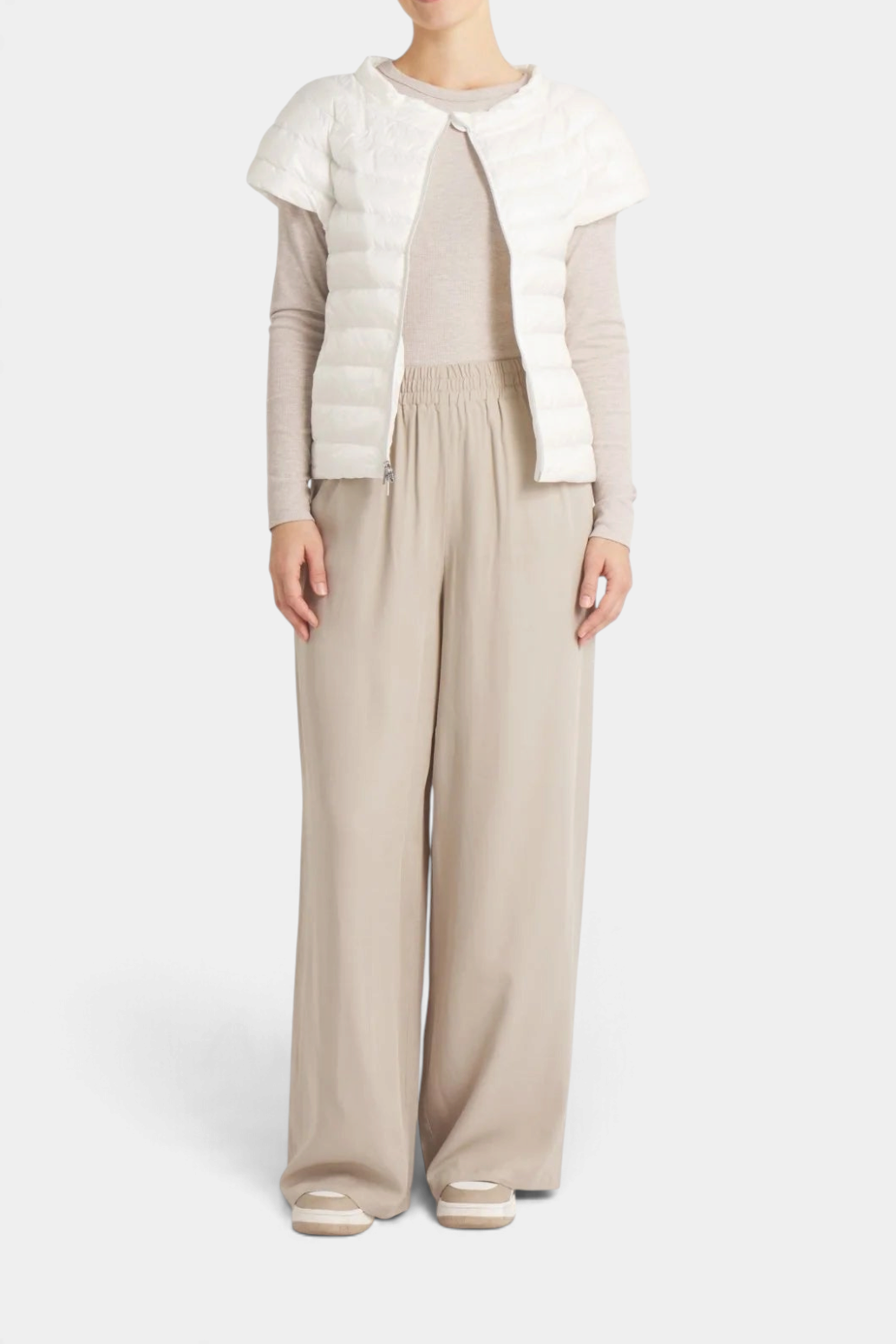 The Copper Shed St Ives white down vest with quarter sleeves worn over a beige long-sleeve top and wide-leg trousers.