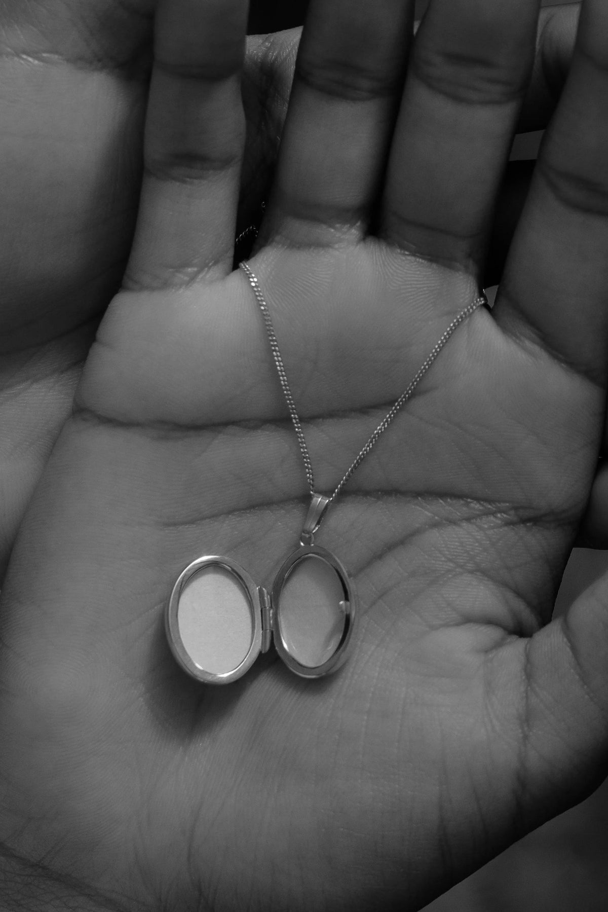The Copper Shed sterling silver oval locket necklace held in a palm, shown open to display space for two photos.