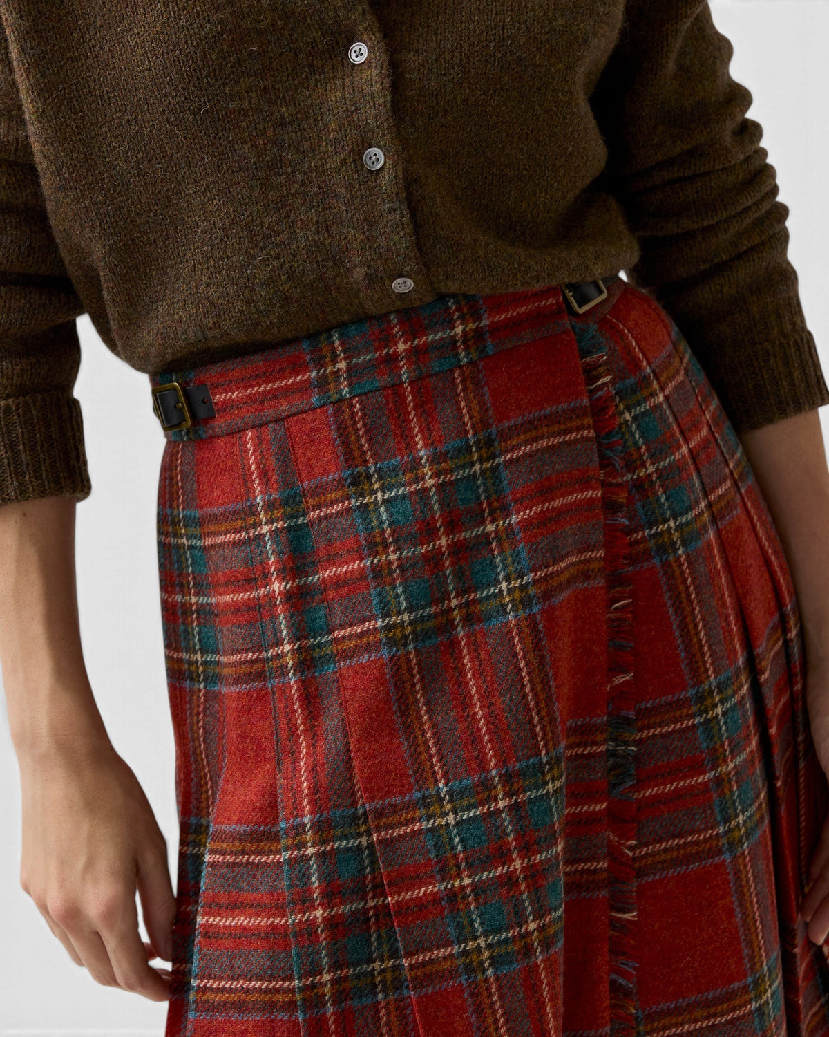 The Copper Shed Royal Stewart tartan wool kilt skirt with adjustable leather side straps worn with a brown sweater.