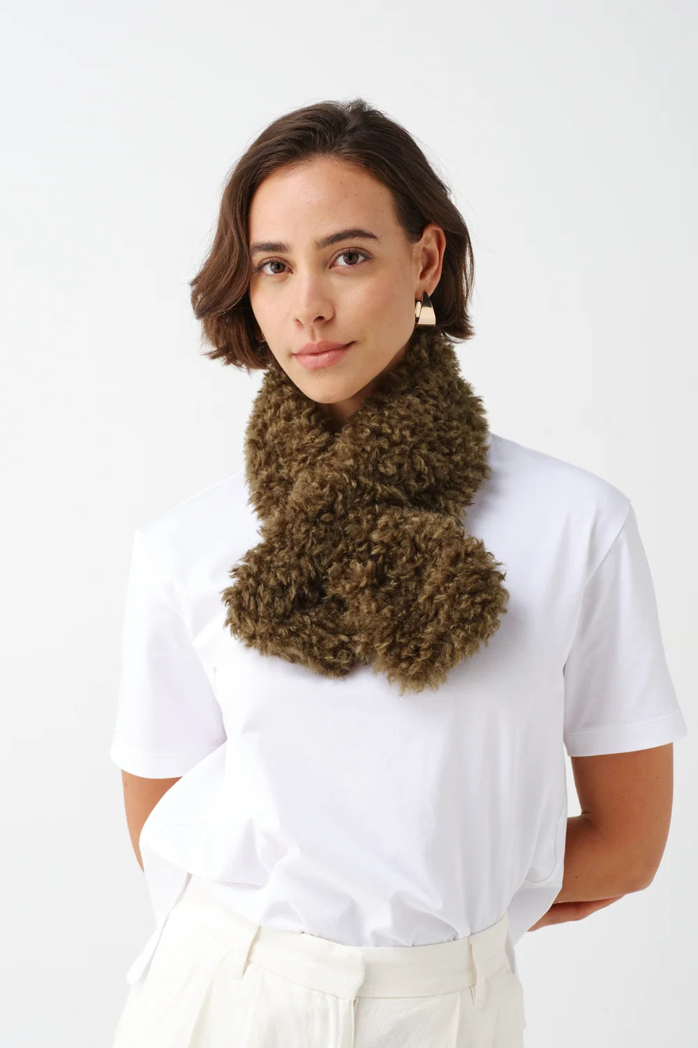 The Copper Shed Tiptop scarf in olive faux sheepskin with a crossover tuck-through design worn by a woman.