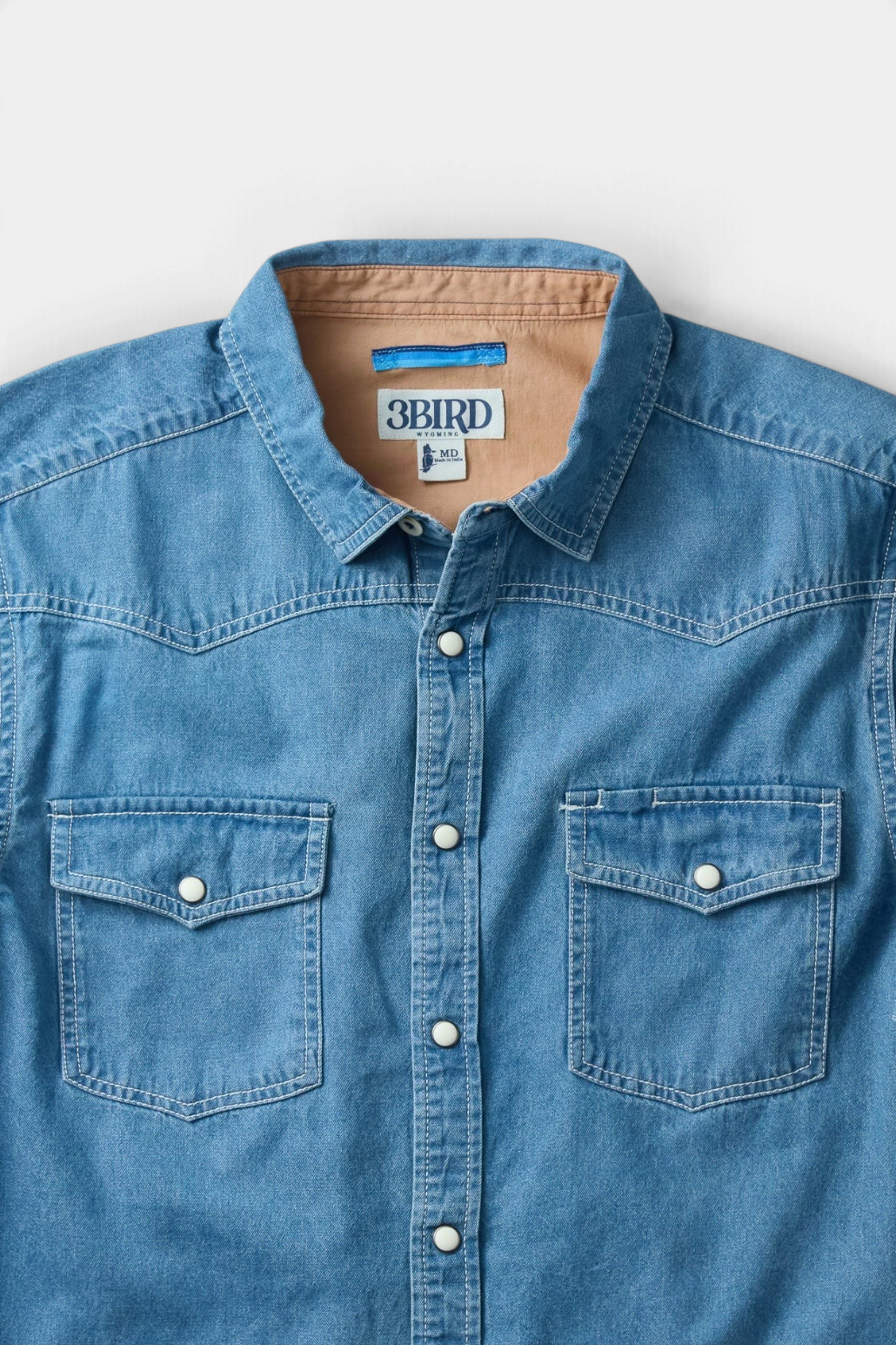 The Copper Shed Westside denim shirt featuring western pearl snaps, dual chest pockets, and a tan chambray collar.