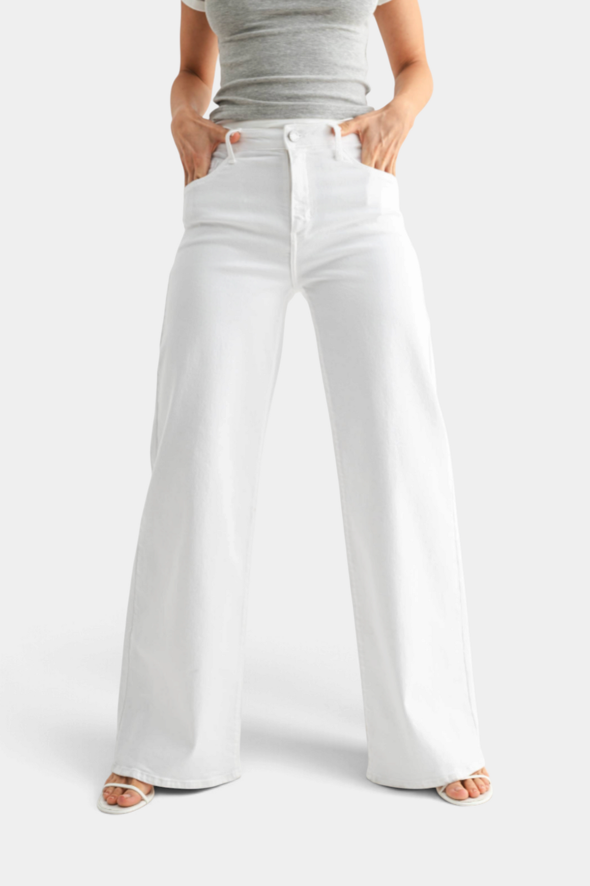 The Copper Shed white stretchy wide leg jeans worn by a model with a grey top and white strappy sandals.