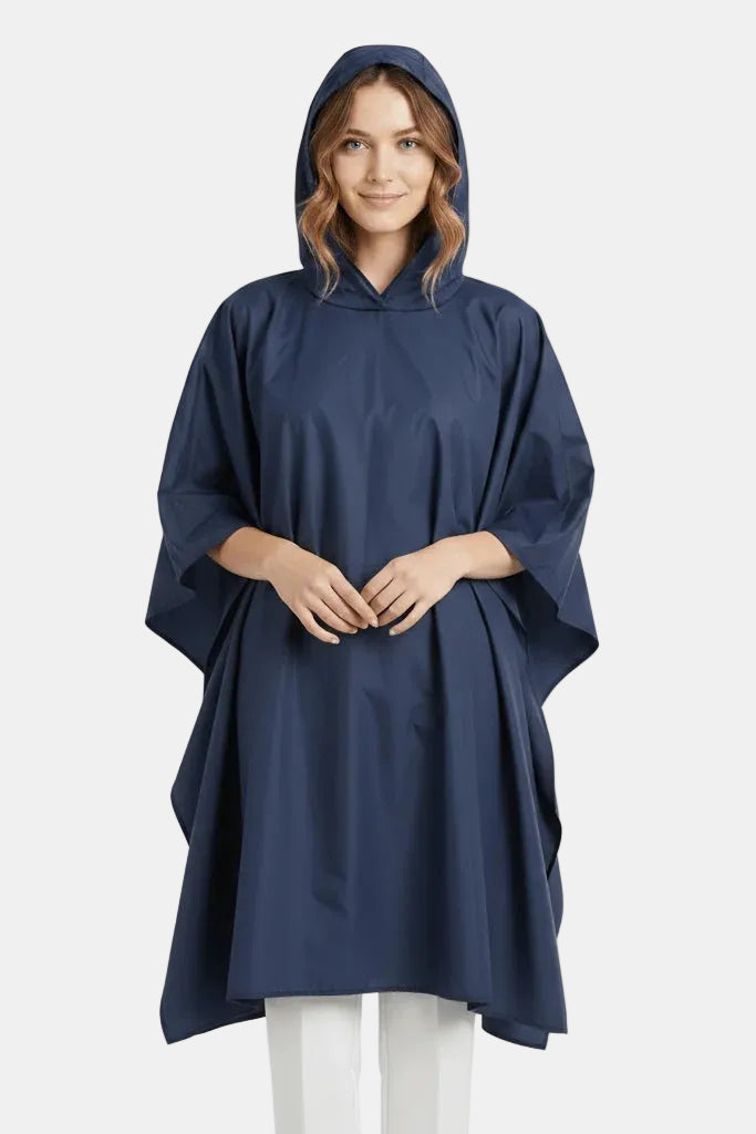 A woman wearing a navy blue hooded poncho raincoat over white pants, standing against a plain white studio background.