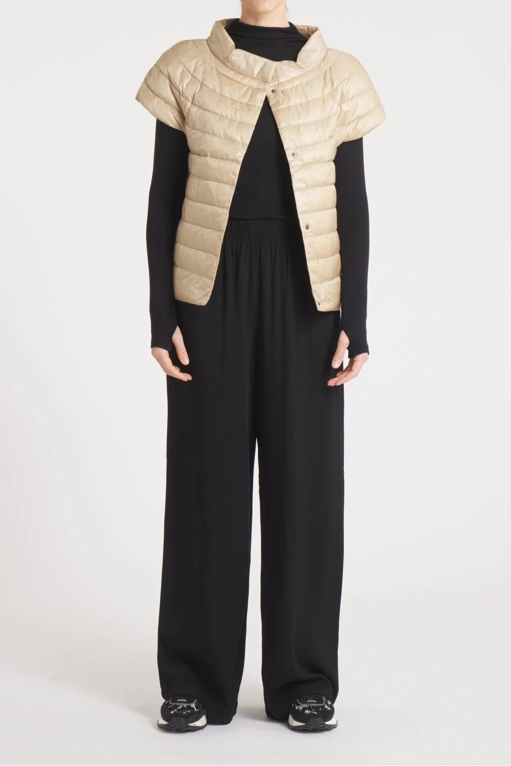 Woman wearing a beige puffer vest over a black outfit on a white background