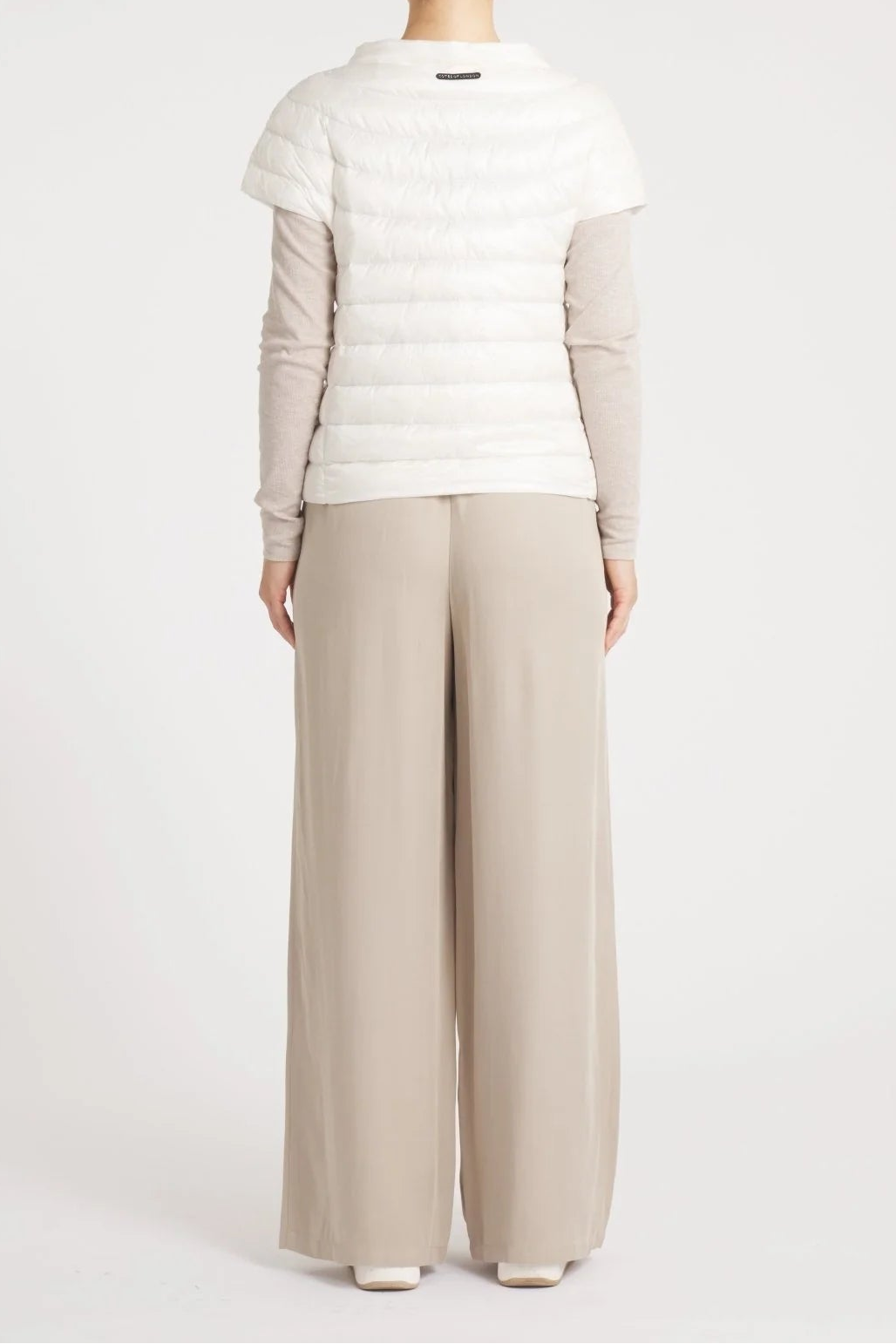 Person wearing a white puffer jacket and beige pants on a white background